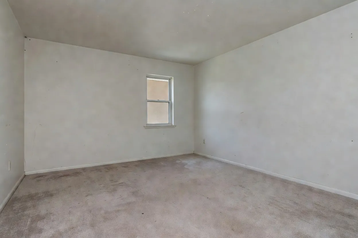 An empty, dated living room with bare walls and old carpet before redesign